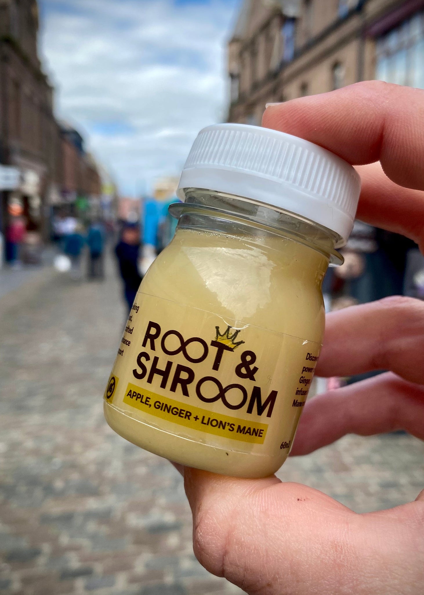 Hand holding a small jar labeled 'Root & Shroom' against a blurred street background