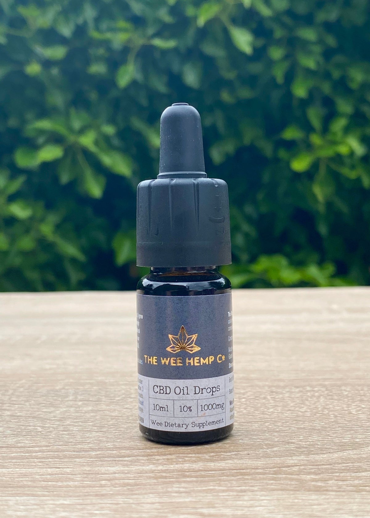CBD oil dropper bottle with 'The Wee Hemp Co.' label on a wooden surface with green foliage in the background. Full Spectrum CBD Oil Drops - 10% | 1000mg - Hemp Oil | Vegan Friendly, Vegetarian Friendly | The Wee Hemp Company CBD Oil Shop | Wee Hemp CBD Oil Shop | Scotland's multi award winning CBD company | CBD Oil Shop | Cannabidiol drops | Aberdeen & Aberdeenshire | CBD Oil, CBD Balm, CBD Vapes E-liquid, CBD Cream, CBD Full Spectrum CBD Oil, Broad Spectrum CBD Oil, 3rd party lab tested CBD Oil
